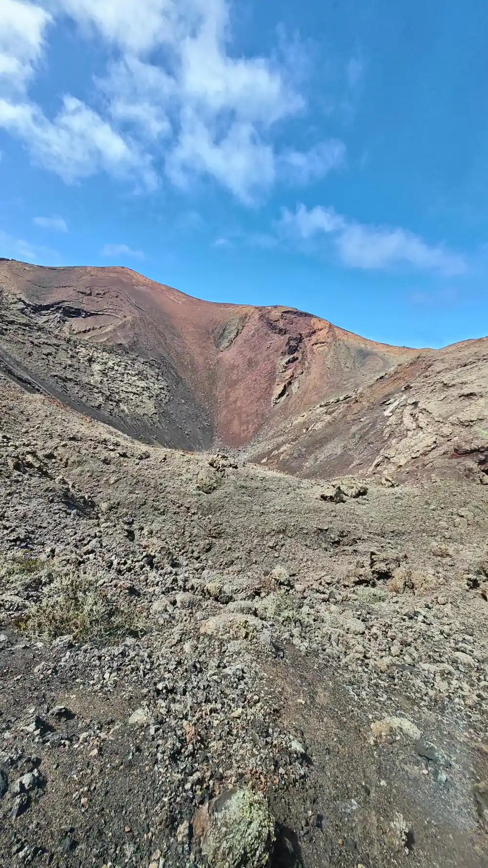 Arid volcanic crater with reddish cinder cone and scree