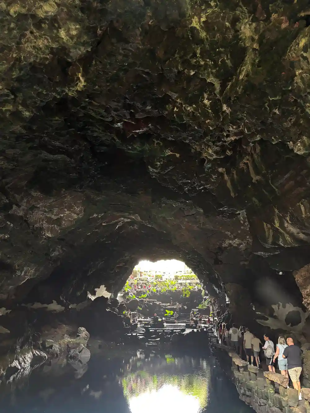 Cave tunnel with water reflecting light, visitors visible ahead