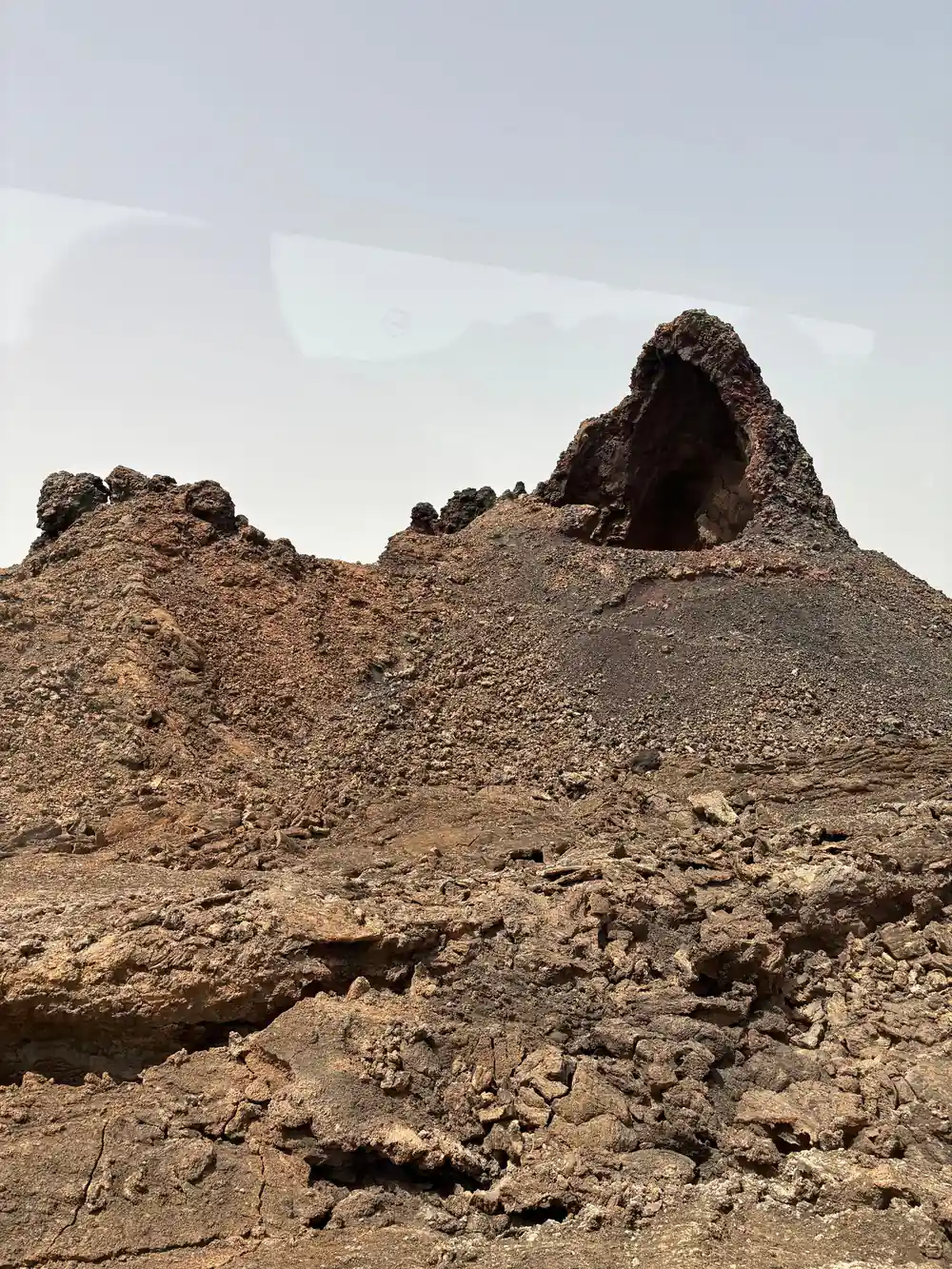 Conical volcanic crater covered in dark reddish-brown cinder