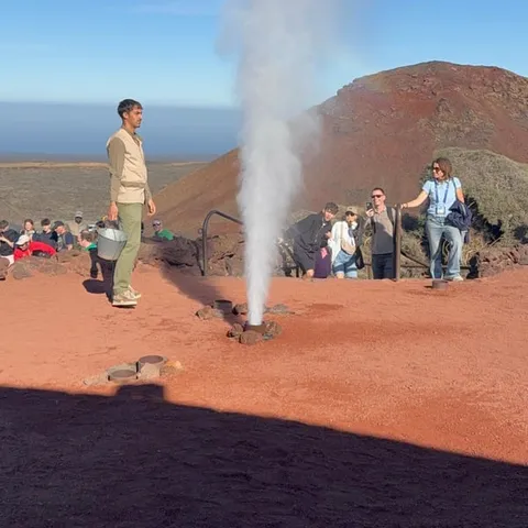Steam geyser shooting up in front of visitors on red ground