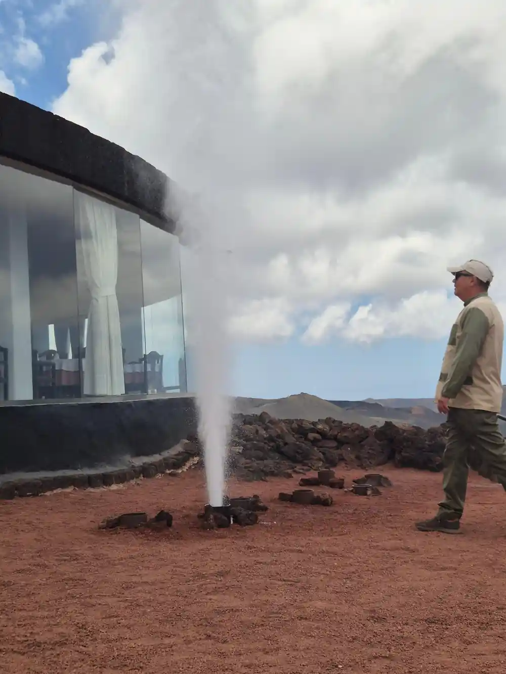 Geyser erupting with person and building nearby for scale