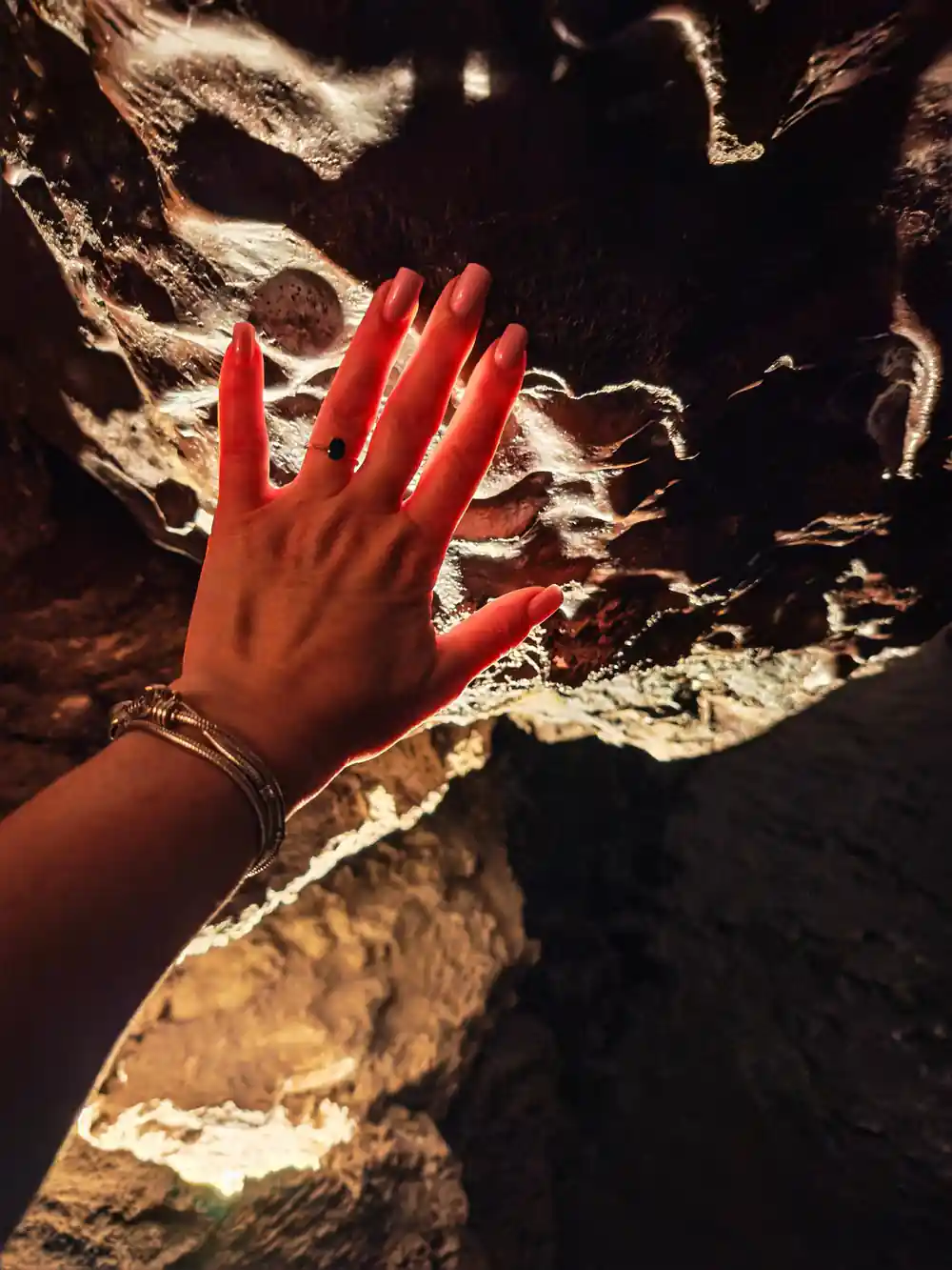 Hand with red nail polish touching cave wall minerals
