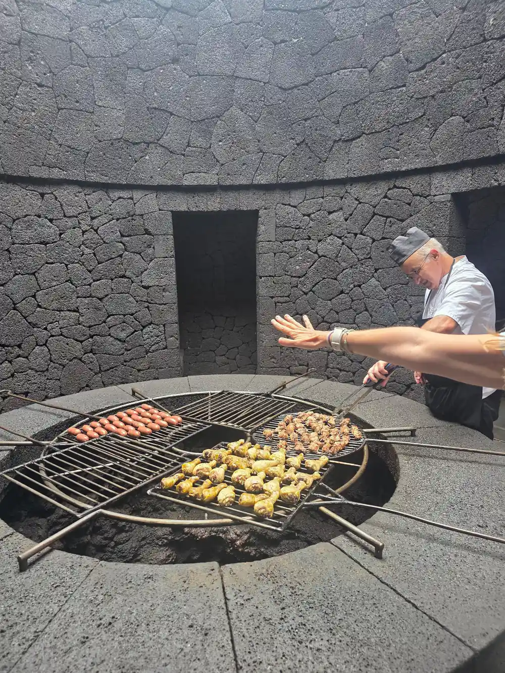 Man cooking meat and vegetables on volcanic ground grill