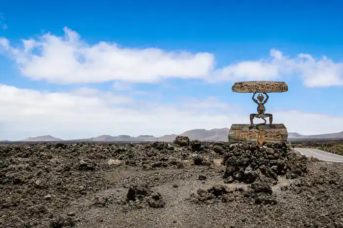 Metal sculpture of figure holding disc on lava field