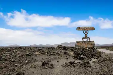 Metal sculpture of figure holding disc on lava field