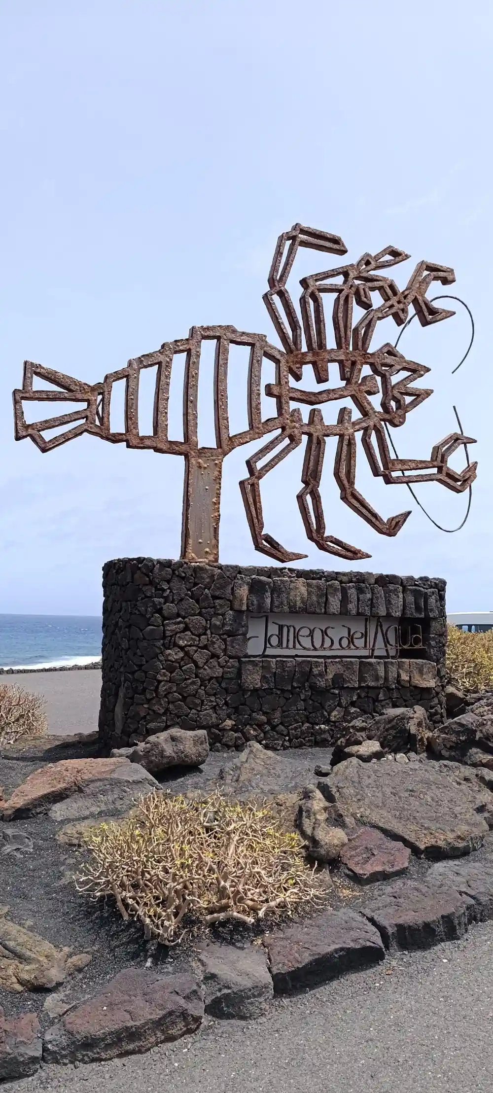 Metal sculpture of octopus-like creature on rocky beach