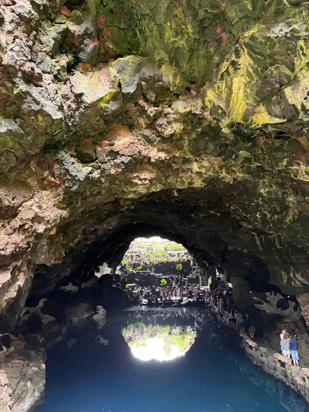 Natural rock tunnel opening to sunlit landscape with water