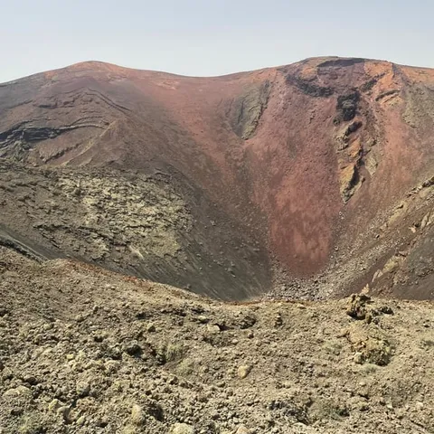 Red and brown volcanic crater under a pale sky