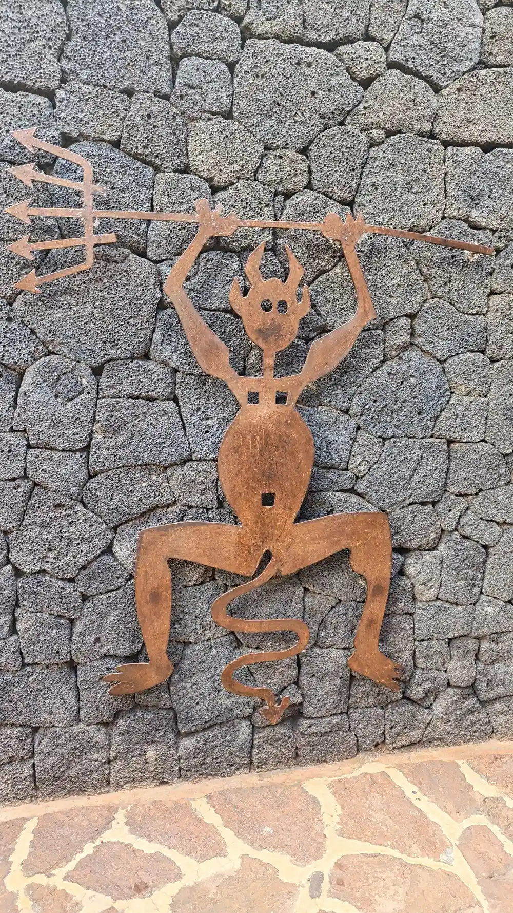 Rusted metal figure sculpture on lava rock wall