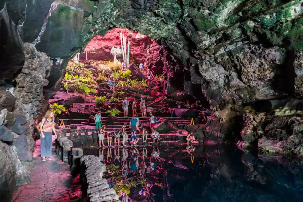 Tourists in cave with pink-lit walls and water pool