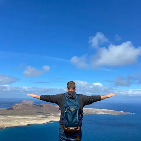 Traveller with arms open on a viewpoint above the coast