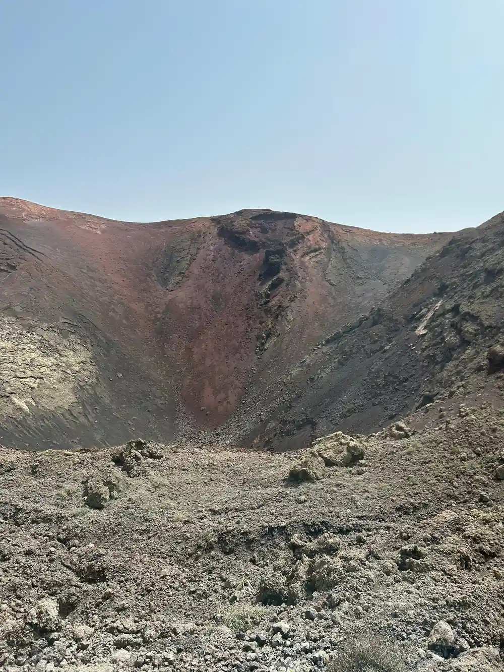 Volcanic crater with reddish-brown rock walls and sparse vegetation