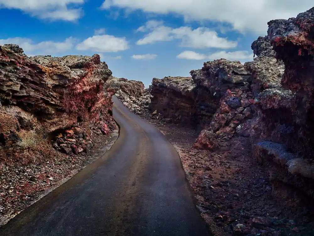 Winding dark asphalt road through red lava rock formations