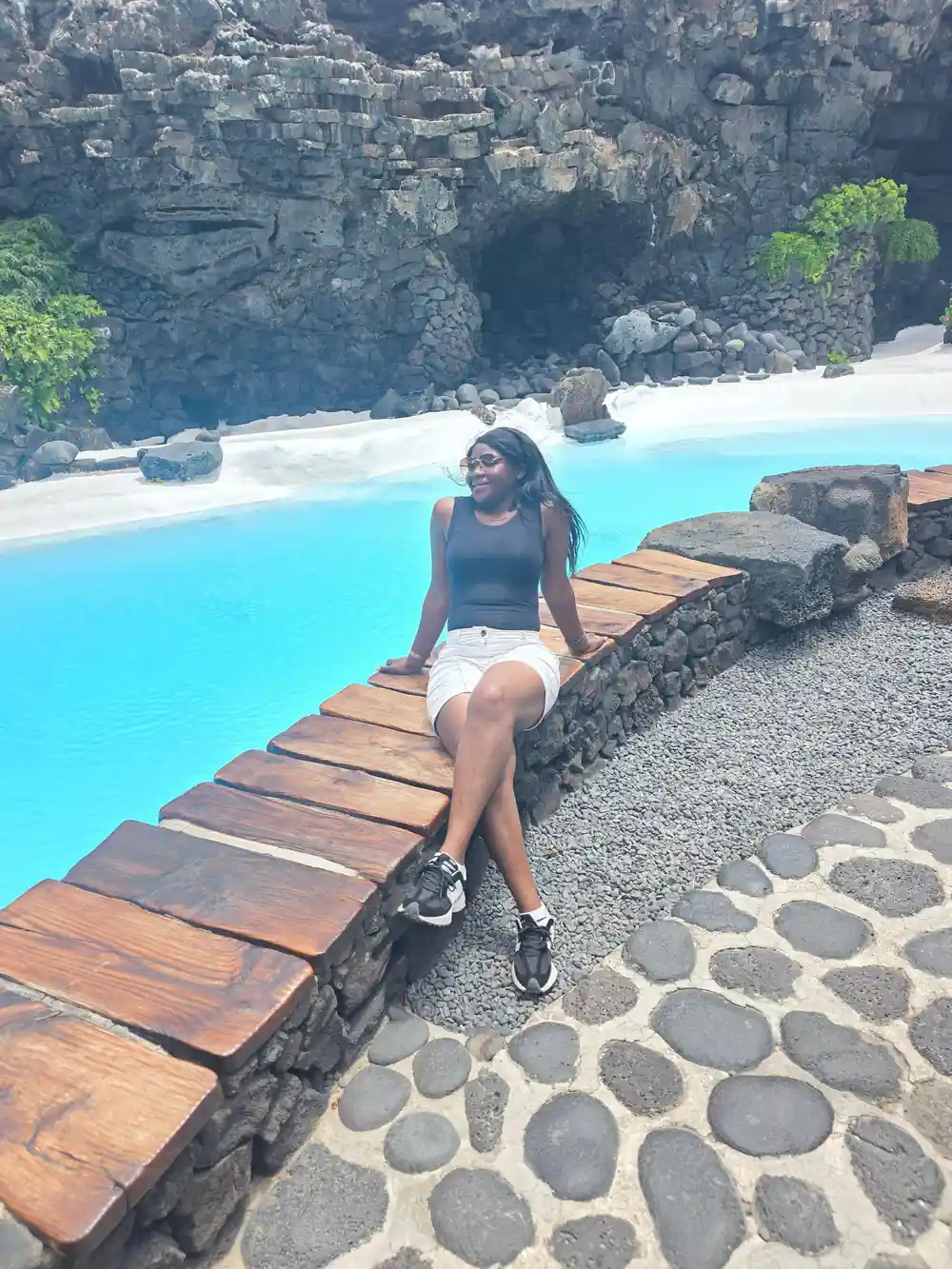 Woman sitting on wooden boardwalk by turquoise pool